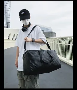 Grand sac de voyage tissé noir porté par un modèle pour le sport et les voyages.