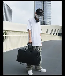Grand sac de voyage tissé noir porté par un mannequin dans un décor urbain
