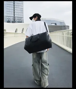 Vue arrière d'un modèle portant un grand sac de voyage tissé noir sur un pont