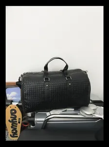 Détail de la texture en cuir tressé noir sur un grand sac de voyage premium.