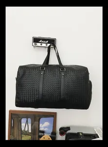 Grand sac de voyage tissé noir suspendu au mur, idéal pour les affaires ou le sport.