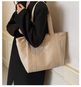 Detalle de bolso tote beige minimalista de gran capacidad con abrigo negro elegante.