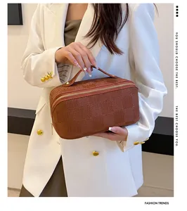 Model holding a brown checkered rectangular makeup bag with handle and gold zipper detail