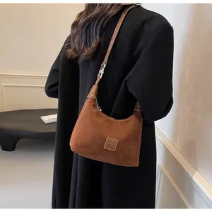 Dettaglio di una borsa sottobraccio in pelle scamosciata marrone indossata da una modella