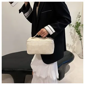 Elegant cream checkered square handbag with handle held by model in minimalist setting