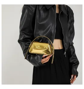 Dettaglio di una mini borsa baguette dorata lucida con giacca di pelle nera.