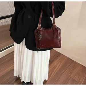 Detail shot of a retro burgundy tote bag styled with a black blazer and white skirt.