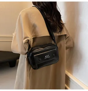 Bolso bandolera negro minimalista con logo BÙF sobre una gabardina color beige
