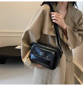 Detalle de un bolso bandolera negro minimalista llevado sobre una gabardina beige