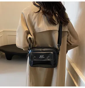 Bolso bandolera cuadrado negro moderno combinado con una gabardina beige para un look chic.