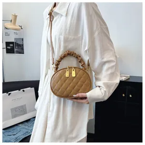 Detail shot of a stylish tan quilted handbag featuring a ruched handle and gold zippers.