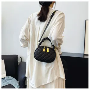 Model wearing a black quilted crossbody bag with gold hardware and ruffled handle details.