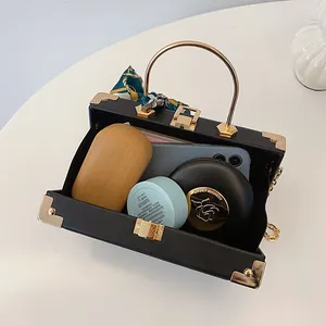 Elegante zwarte box-tas in kofferstijl met goudkleurig handvat en zijden sjaal