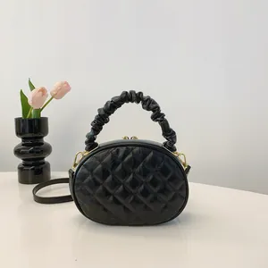 Close-up detail of black quilted oval handbag featuring unique ruched handle and gold accents