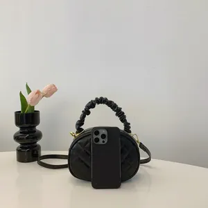 Elegant black quilted crossbody bag with ruffled handle shown next to a smartphone for size