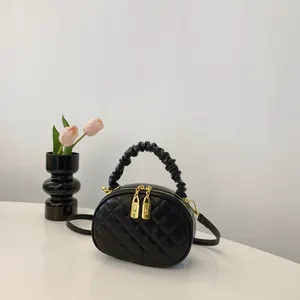 Detail view of a stylish black quilted handbag with a ruffled handle and gold zippers