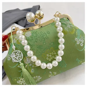 Detalle de bolso bordado chino vintage verde con elegante asa de perlas decorativas.