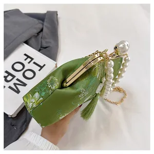 Primer plano de bolso chino bordado verde con asa de perlas y borla elegante
