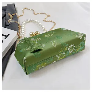 Detalle de un bolso de fiesta bordado verde con asa de perlas y borla.