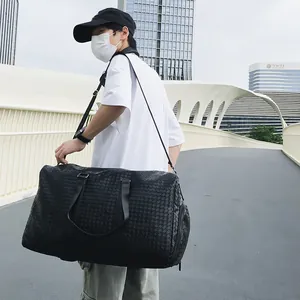 Grand sac de voyage noir tissé avec compartiment à chaussures porté par un mannequin.