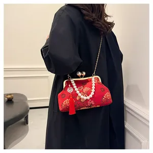 Detalle de un bolso bordado rojo de estilo chino con asa de perlas y cadena dorada