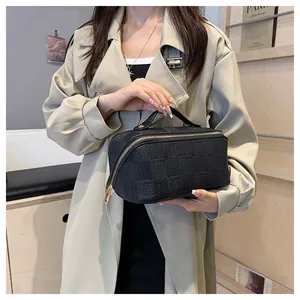Detailed view of a black checkered makeup bag held by a model in a stylish trench coat.