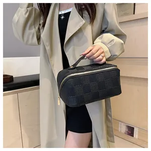 Detail of black checkered square cosmetic bag with golden zipper held by model