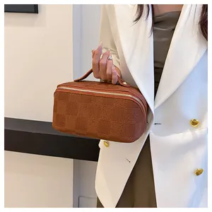 Detailed view of a stylish brown checkered portable makeup bag with gold zipper held by a model