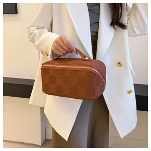 Close-up of a brown checkered portable cosmetic bag held by a model in a white blazer