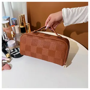 Elegant brown checkered vanity bag with top handle and zipper closure being held by a hand