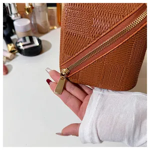 Close-up detail of a brown woven checkered cosmetic bag showing premium gold zipper pull