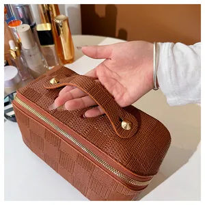 Detailed view of a hand holding the handle of a brown woven plaid vanity makeup storage bag