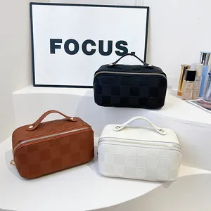 Three checkered square cosmetic bags in black, brown, and white with top handles.