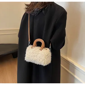 Detailed shot of a white plush crossbody bag with brown leather straps worn on a black coat