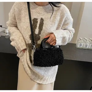 Detailed shot of a black fuzzy plush handbag featuring a top handle and long strap.