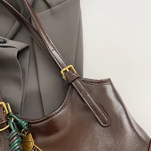 Close-up detail of glossy brown leather bag with gold-tone buckle and braided charm