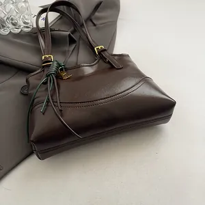 Close-up of a vintage brown tote bag with decorative key charm and green leather tie.