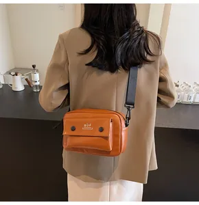 Detalle de bolso bandolera cuadrado naranja llevado por una modelo en un café.