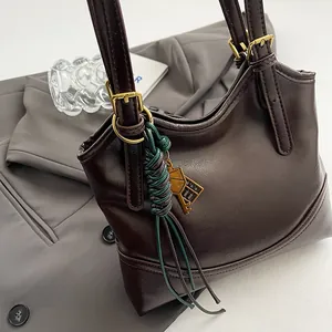 Close-up of a vintage brown leather tote bag with a decorative green charm and gold buckles.