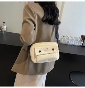 Vista detallada de un bolso bandolera cuadrado crema minimalista en una modelo