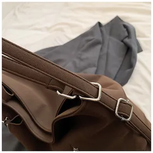 Gros plan d'une bandoulière de sac marron avec boucles en métal argenté et coutures fines