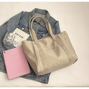 Vista detallada de un bolso tote de nailon beige sobre una chaqueta vaquera con accesorios.