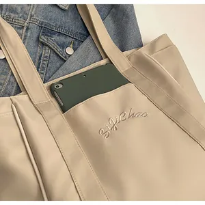 Primer plano de un bolso tote de nailon beige con bolsillo delantero y bordado de logotipo