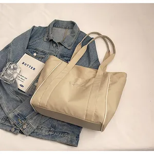 Primer plano de un bolso tote de nailon beige con bordados y ribetes laterales