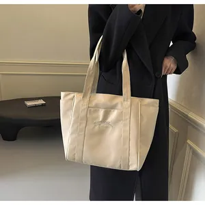 Detalle de un elegante bolso tote de nailon crema llevado por una modelo con abrigo