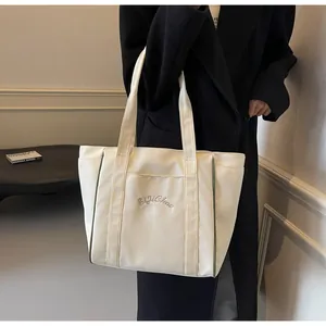 Primer plano detallado de un bolso tote de nailon crema con bordado elegante para oficina