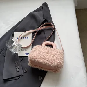 Close-up of elegant pink plush box handbag with leather strap resting on a grey blazer