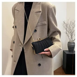 Close-up of elegant black pleated evening clutch with gold ring clasp and chain
