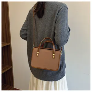 Détail en gros plan d'un sac à bandoulière patchwork marron porté avec un pull gris