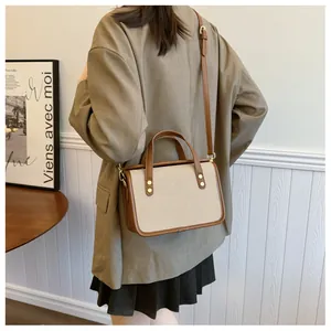 Élégant sac à bandoulière minimaliste en toile beige et cuir marron porté par un mannequin.